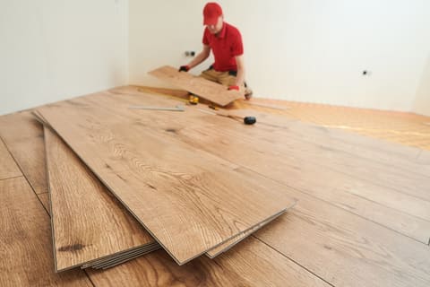 Handwerker verlegt Bodenbelag in Holzoptik in einem hellen Raum