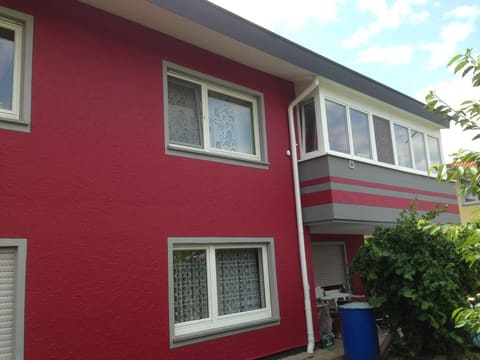Hausfassade in kräftigem Rot mit grau abgesetzten Fensterfaschen